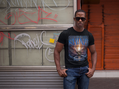 Man wearing a black t-shirt with a graphic design in front of a graffiti-covered wall.